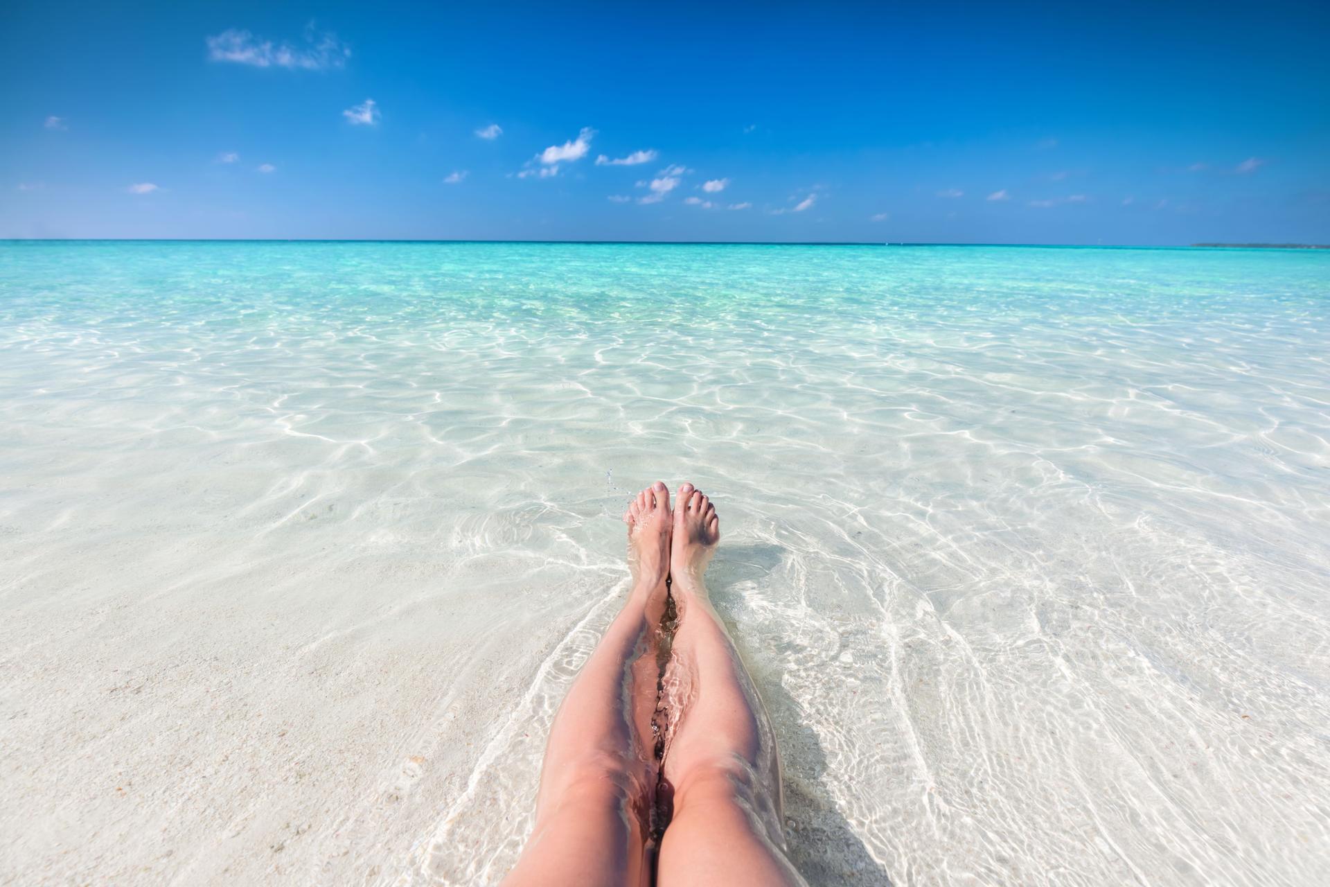 Vacation on tropical beach in Maldives. Woman's legs in the clear ocean